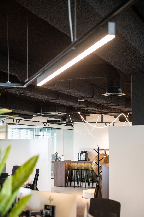 Kantoor in Roeselare met een zwart gespoten Zenko-plafond, lichtlijnen en een open keuken op de achtergrond